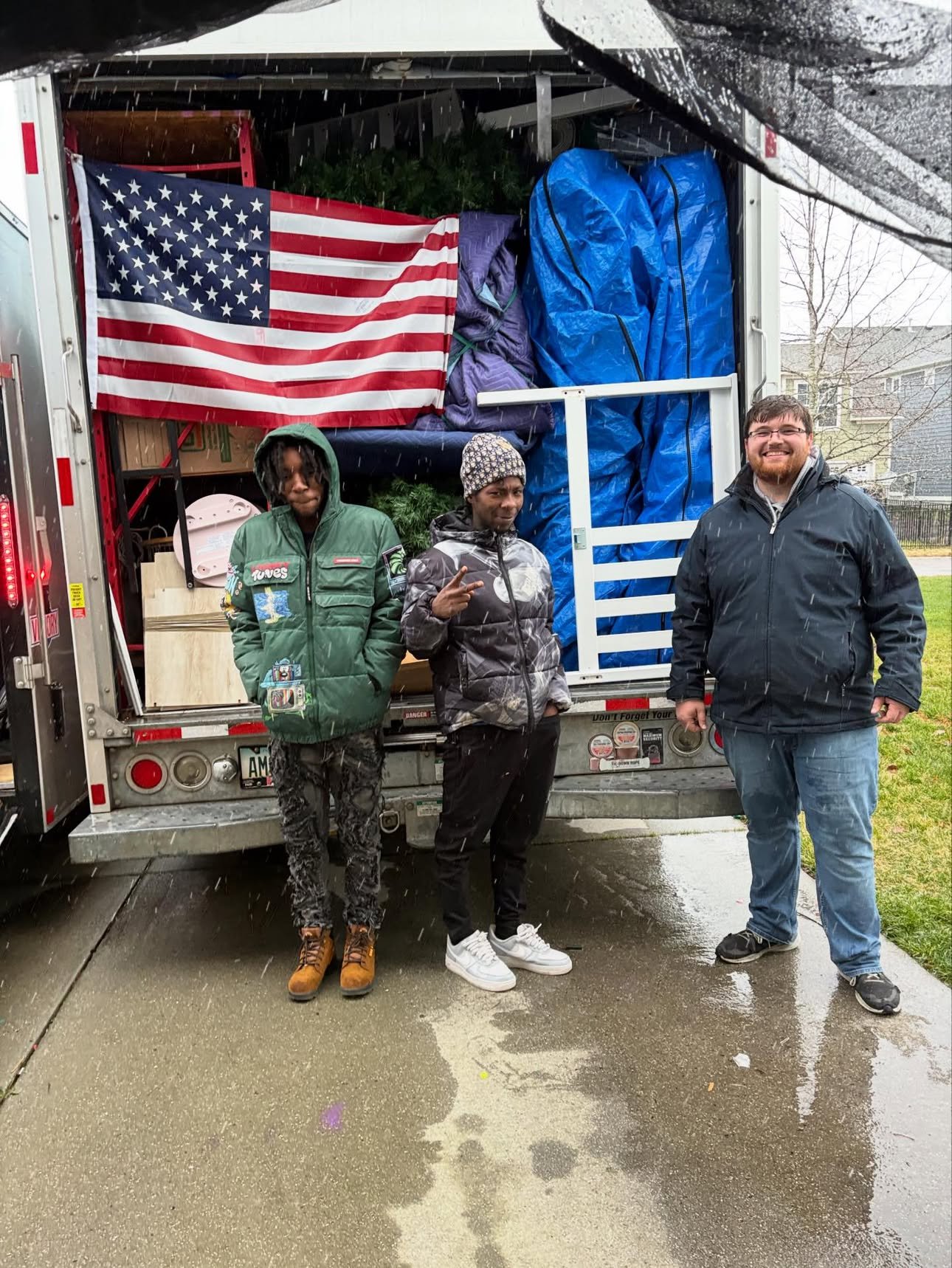 The Anchor Arm Moving crew at the back of a loaded moving truck with a large American flag hung inside, on a rainy Hampton Roads move day