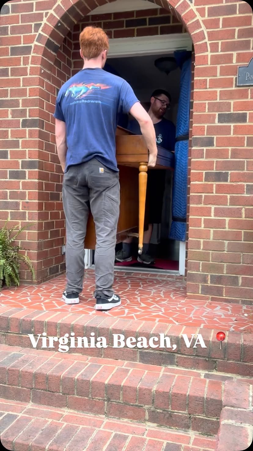 Two Anchor Arm movers carrying a piece of furniture up brick steps into a home in Virginia Beach